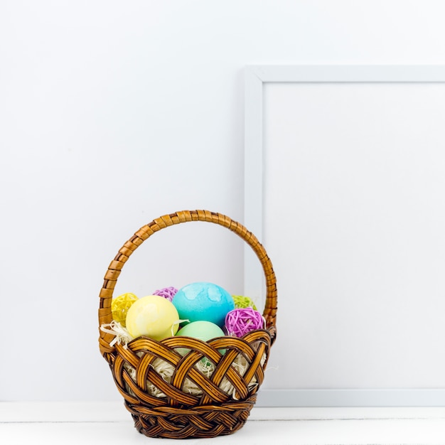 Basket with Easter eggs near frame on table