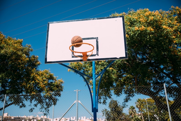 Basketball falling into hoop on blue sky