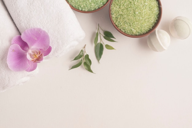 Bath bombs, herbal sea salt and rolled up towels with orchid on white backdrop