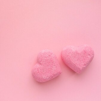 Бомбочки для ванны в форме сердца на розовом фоне, вид сверху.