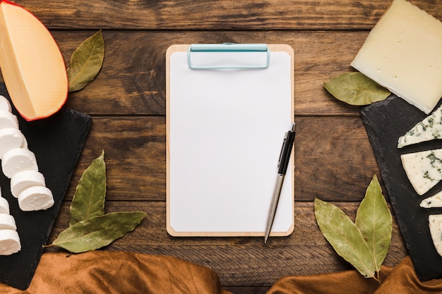 Bay leaves; cheese; cloth; pen and clipboard on wooden desk