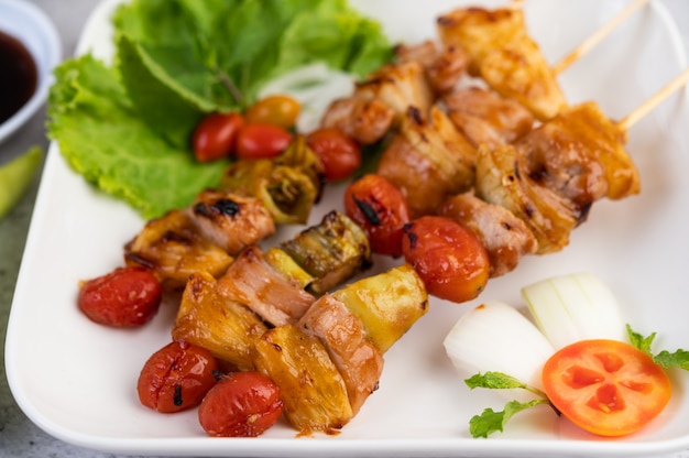 Барбекю с разнообразным мясом, в комплекте с помидорами и сладким перцем на белой тарелке.