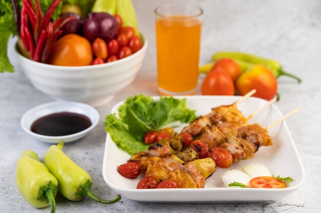 BBQ with a variety of meats, complete with tomatoes and bell peppers on a white plate.