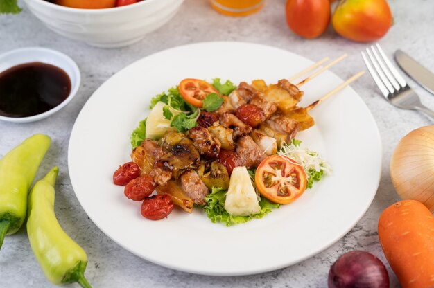 BBQ with a variety of meats, complete with tomatoes and bell peppers on a white plate.