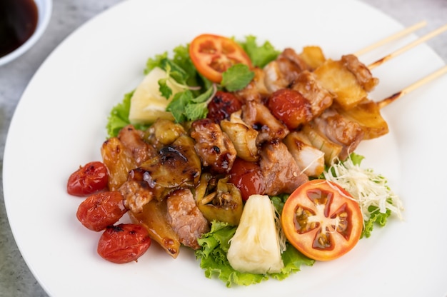 BBQ with a variety of meats, complete with tomatoes and bell peppers on a white plate.