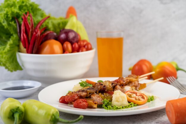 BBQ with a variety of meats, complete with tomatoes and bell peppers on a white plate.