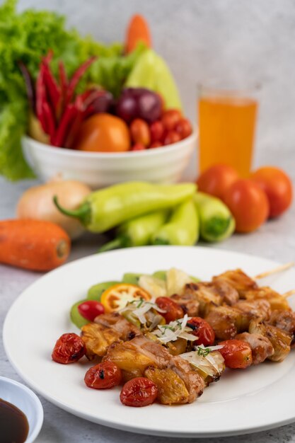 BBQ with a variety of meats, complete with tomatoes and bell peppers on a white plate.