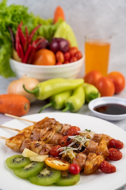 BBQ with a variety of meats, complete with tomatoes and bell peppers on a white plate.