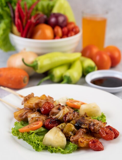 BBQ with a variety of meats, complete with tomatoes and bell peppers on a white plate.