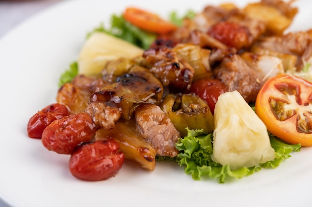 BBQ with a variety of meats, complete with tomatoes and bell peppers on a white plate.