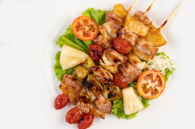 BBQ with a variety of meats, complete with tomatoes and bell peppers on a white plate.