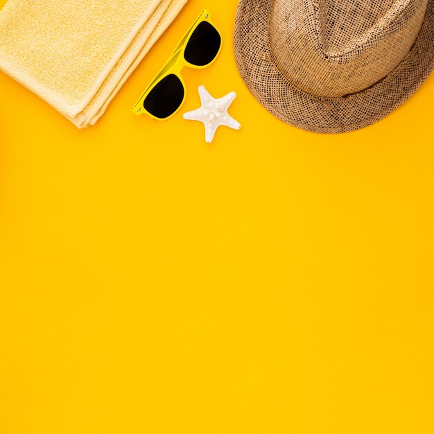 黄色の背景にビーチアクセサリー。ヒトデ、サングラス、タオル、縞模様の帽子。