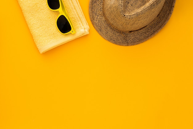 Foto gratuita accessori da spiaggia sullo sfondo giallo. occhiali da sole, asciugamano infradito e cappello a righe.