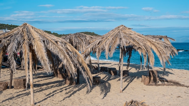 Beach of the Aegean sea with umbrellas made of palm branches  in Greece