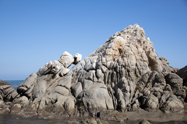 日光とメキシコの青い空の下で海に囲まれた岩に覆われたビーチ