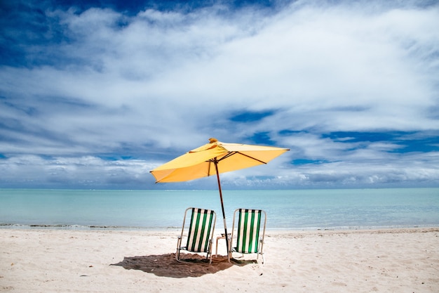 Пляжный зонтик и зеленые шезлонги на берегу