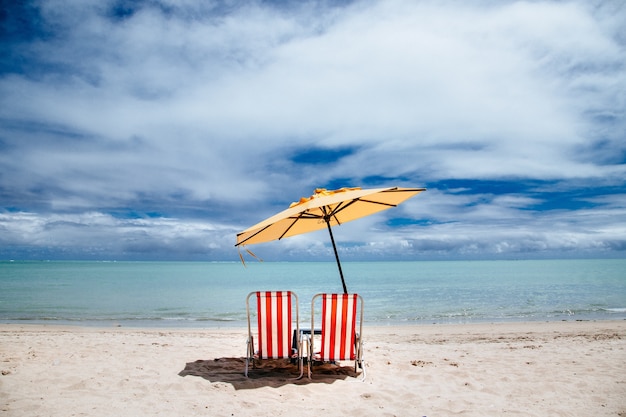Пляжный зонтик и красные шезлонги на берегу
