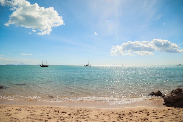 日光の下で丘とその上に船と海に囲まれたビーチ