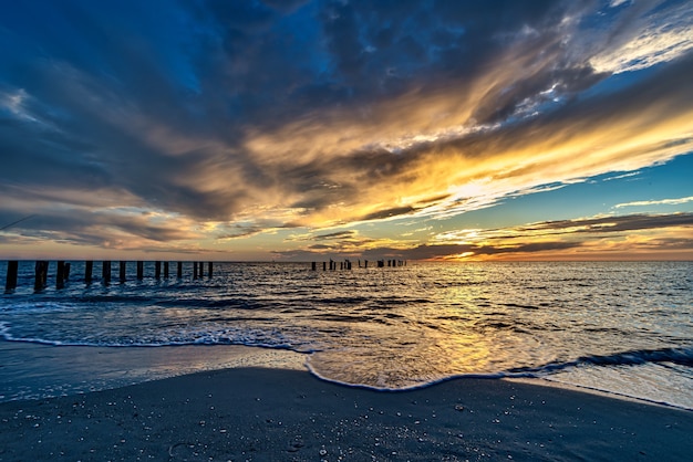 Beach surrounded by the sea with vertical wooden planks in it during the sunset in the evening