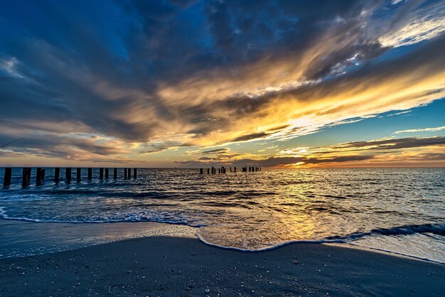 Beach surrounded by the sea with vertical wooden planks in it during the sunset in the evening