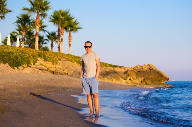 해변 여행 - 모래 해변에 서 있는 젊은 남자