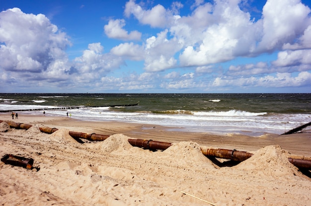 Пляж на курорте Устроне Морские в Польше, большая ржавая труба на песчаном пляже на переднем плане