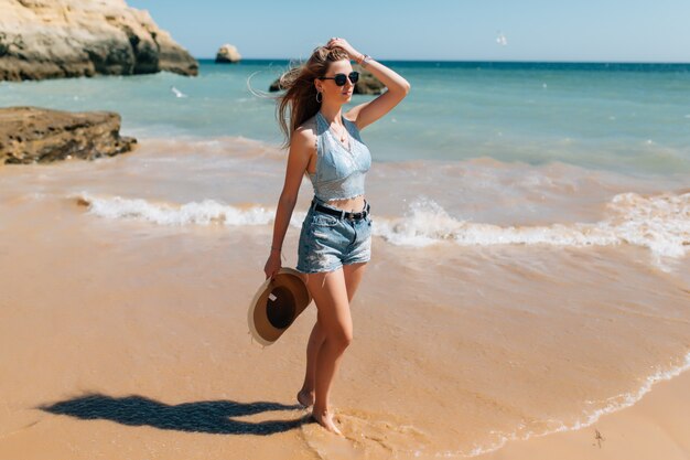 Beach vacation. Beautiful woman in sunhat enjoying perfect sunny day walking on the beach. Happiness and bliss.