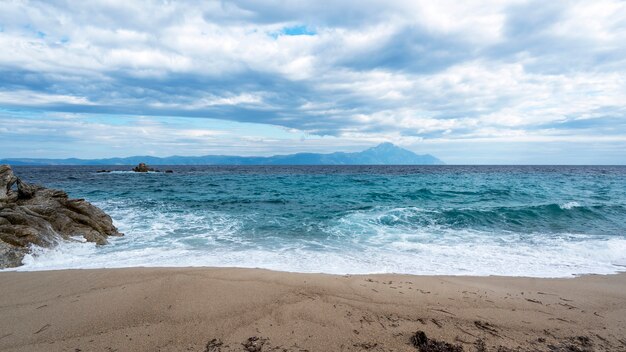 A beach with rocks and blue waves of the Aegean sea, land and mountain