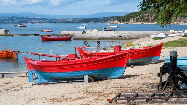 Beached wooden colored boats on Aegean sea cost, pier, yachts and hills in Ouranoupolis, Greece