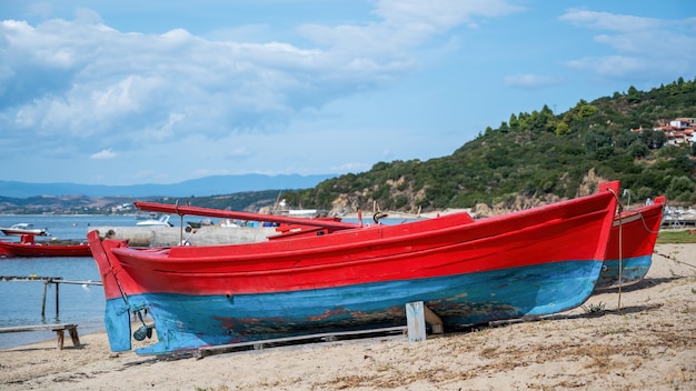 Beached wooden colored boats on Aegean sea cost, pier, yachts and hills in Ouranoupolis, Greece