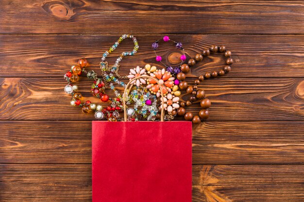 Beads jewelry and red paper bag on wooden background