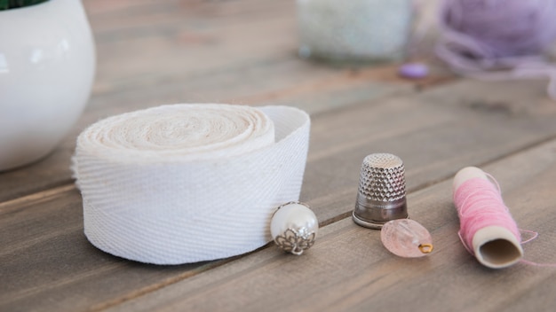 Beads; thimble; white ribbon and pink spool on wooden desk