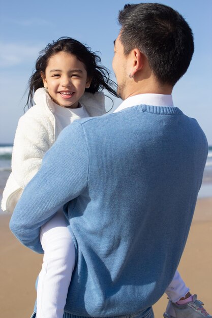 Сияющие отец и дочь на пляже. Японская семья гуляет, обнимается, папа несет маленькую девочку. Досуг, семейное время, концепция воспитания
