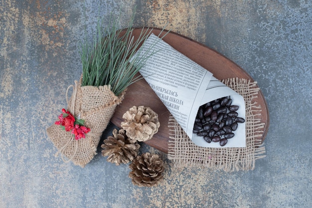 Beans in newspaper with pinecones on wooden board .