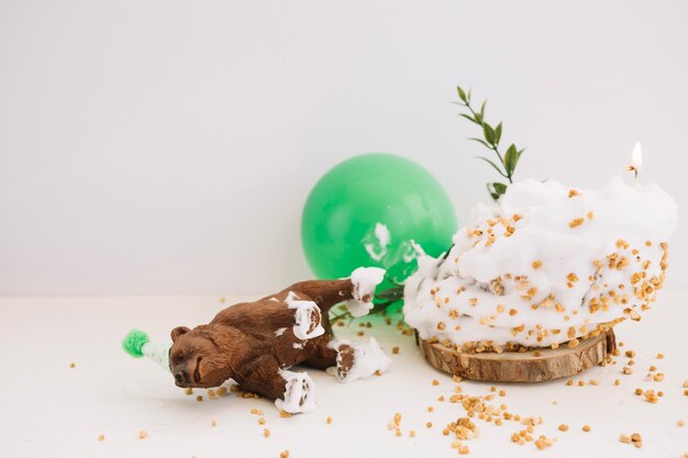 Bear statuette lying near cake and balloon