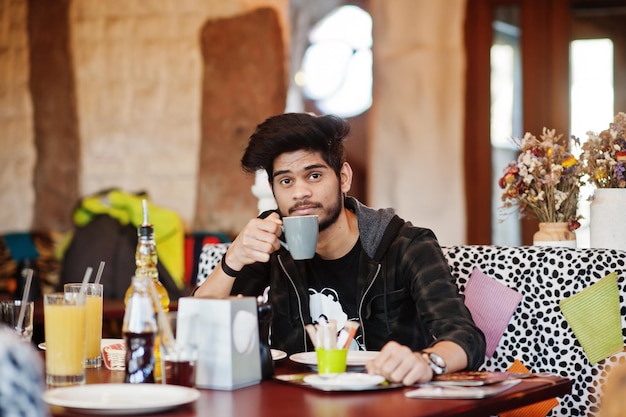 Barba uomo asiatico in abbigliamento casual seduto al bar al coperto e bere caffè