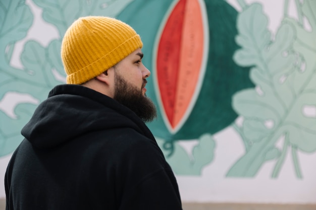 Бесплатное фото Борода человек в трикотажной шляпе, стоящей перед стенами граффити