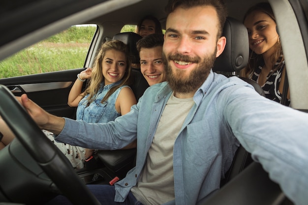 ひげそりの若い男がセルフを取って車に彼の友人と座って