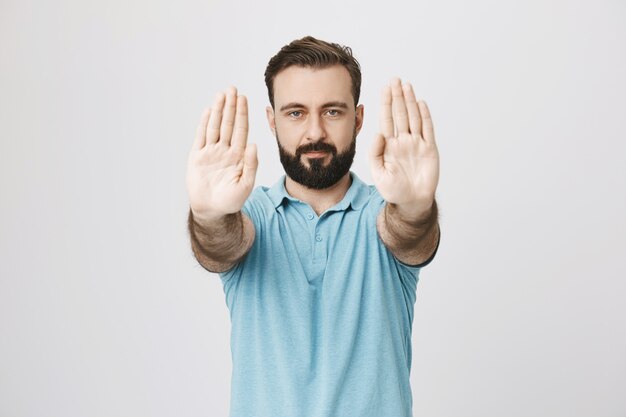 Bearded adult man extend hands forward to show stop sign