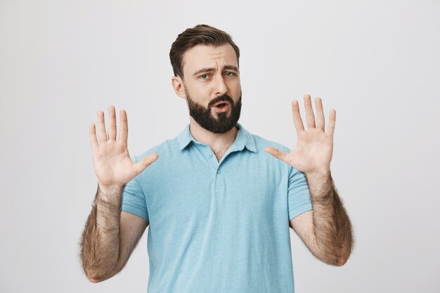 Bearded adult man trying calm down person, raising hands up
