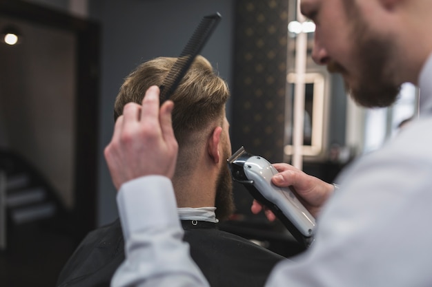 Foto gratuita barbiere barbuto che rade i capelli del cliente