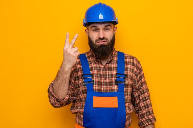 Bearded builder man in construction uniform and safety helmet looking with serious face showing number two with fingers