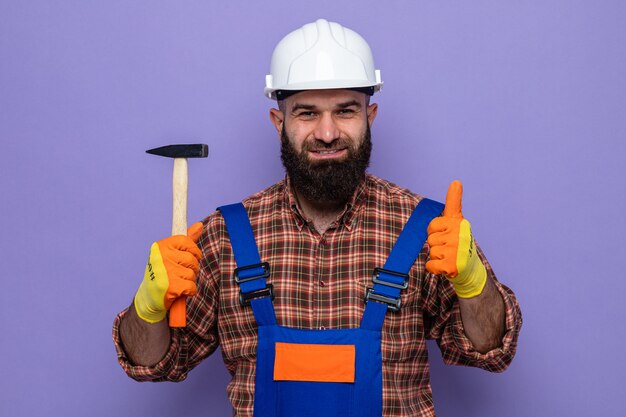 건설 유니폼을 입은 수염 난 건축업자 남자와 고무 장갑을 끼고 고무 장갑을 끼고 엄지손가락을 치켜들며 자신감 있게 웃고 있는 모습