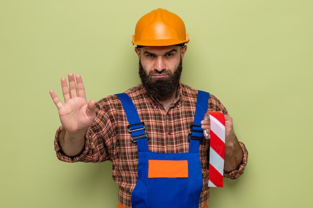 無料写真 建設制服のひげを生やしたビルダーの男と手で停止ジェスチャーを作る深刻な顔で見て粘着テープを保持している安全ヘルメット