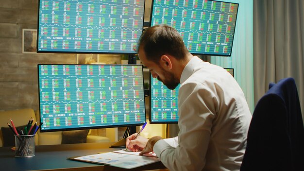 Бородатый бизнесмен делает заметки при проверке фондового рынка из домашнего офиса.