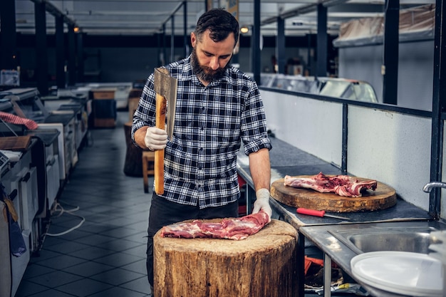 Free photo bearded butcher dressed in a fleece shirt cuts meat with a bloody axe.