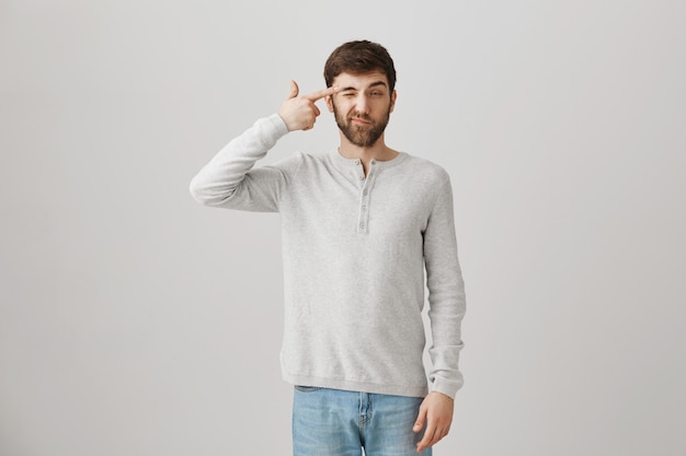 Bearded caucasian guy tired, making gun gesture near temple