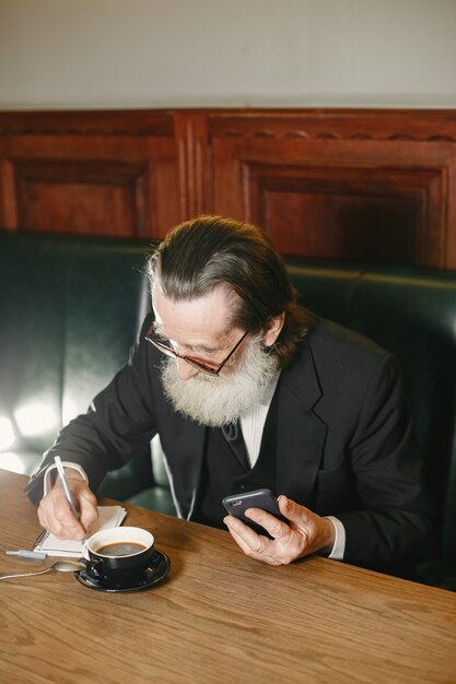 Bearded elderly businessman. Man with coffee. Senior in black suit.