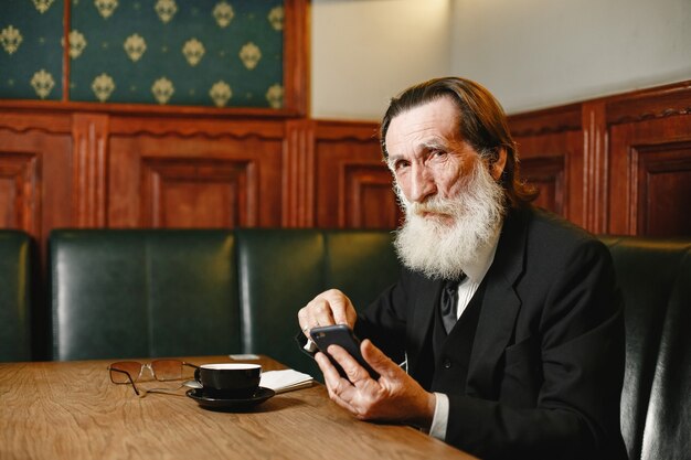 あごひげを生やした年配のビジネスマン。コーヒーを持つ男。黒のスーツを着た先輩。