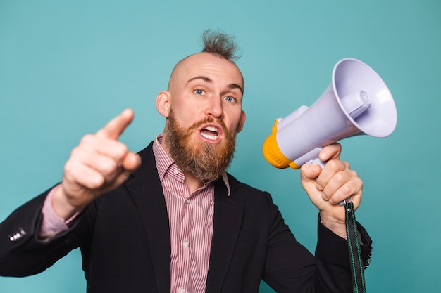 Bearded european businessman in dark suit isolated, with megaphone shouting with serious angry face, asking for attention